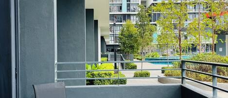 Un balcon avec une table et des chaises en verre, une vue sur un immeuble moderne et un petit espace jardin.