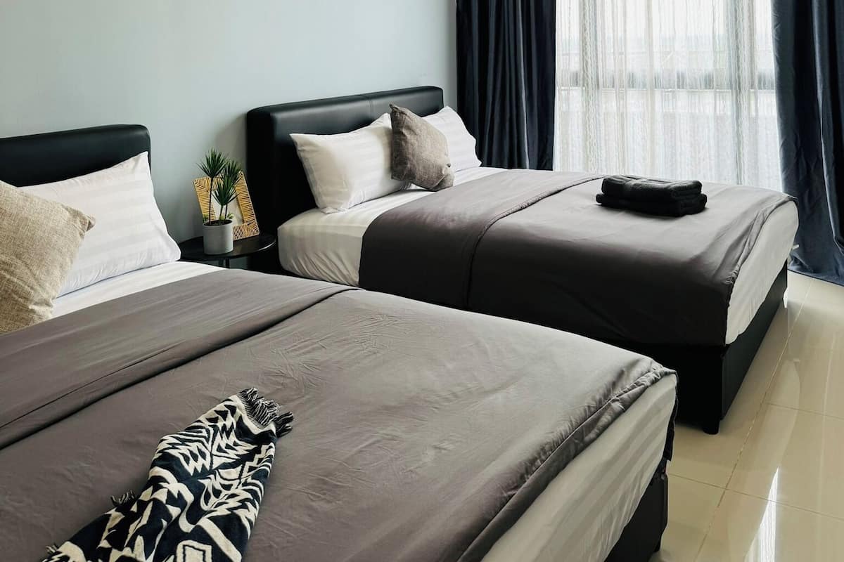 A hotel room with two beds, each with a dark headboard and a neutral-toned bedspread. There is a small potted plant on the nightstand beside one bed.