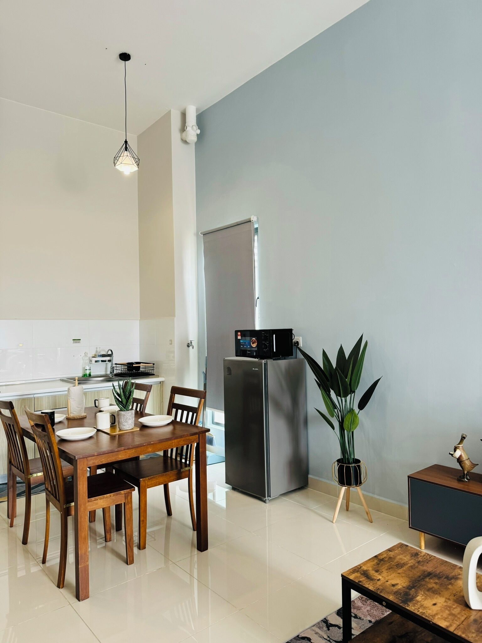 A modern kitchen with a stainless steel refrigerator, a dining table with chairs, and a small side table with a plant.