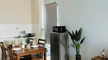 A modern kitchen with a stainless steel refrigerator, a dining table with chairs, and a small side table with a plant.