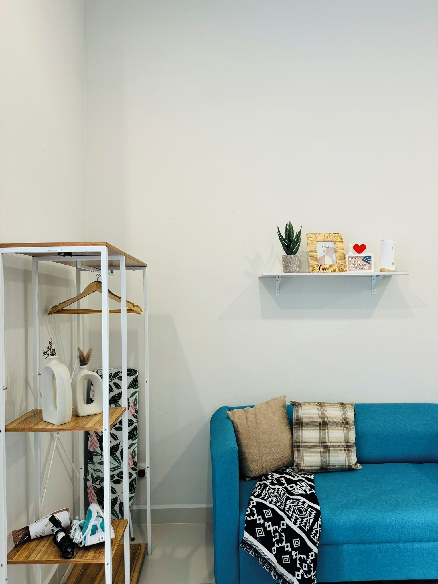 A room with a blue sofa, a wooden shelf unit, and a white wall with a small shelf holding decorative items.