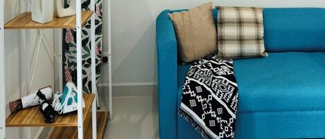 A room with a blue sofa, a wooden shelf unit, and a white wall with a small shelf holding decorative items.