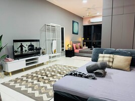 A modern living room with a flat-screen TV, a white entertainment unit, a grey sofa, and a patterned rug.