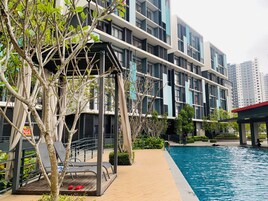A modern building with a swimming pool, outdoor seating, and greenery.