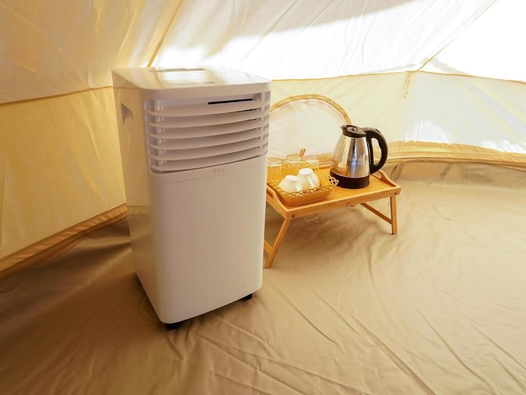 Un chauffage portable, une machine à café et un plateau avec des tasses et un thermos à l’intérieur d’une tente.