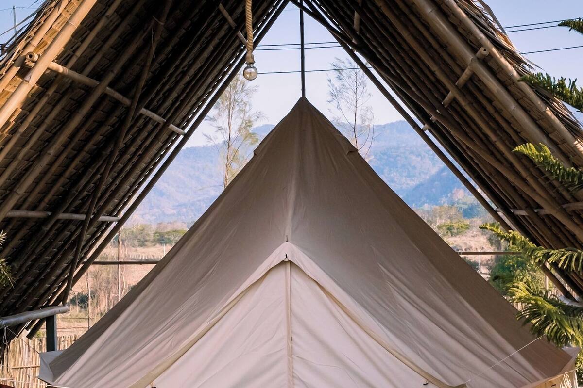 Una tenda gran i blanca amb teulat a dos vessants, instal·lada en una zona oberta amb vistes a les muntanyes al fons.