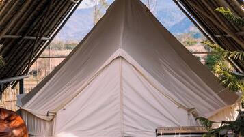 A large, white tent with a peaked roof, set up in an open area with a view of mountains in the background.