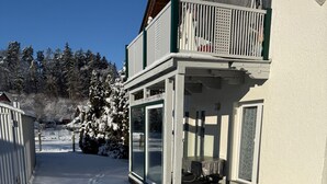 A two-story building with a balcony, a covered outdoor seating area, and a snow-covered ground. - Ferienwohnung für Max. 2 Personen (Tacherting)