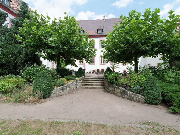 Un bâtiment doté d’un escalier en pierre menant à une porte, entouré d’une végétation luxuriante et sous un ciel dégagé.