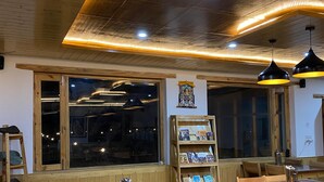 A cozy restaurant interior with wooden furniture, pendant lighting, and a view through large windows. - Rangjon Resort (Leh)