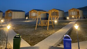 A row of wooden cabins with attached porches, a swing set, and a pathway with street lamps. - Rangjon Resort (Leh)