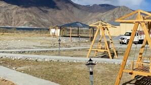 A desert landscape with mountains in the background, wooden swings, and a clear blue sky. - Rangjon Resort (Leh)