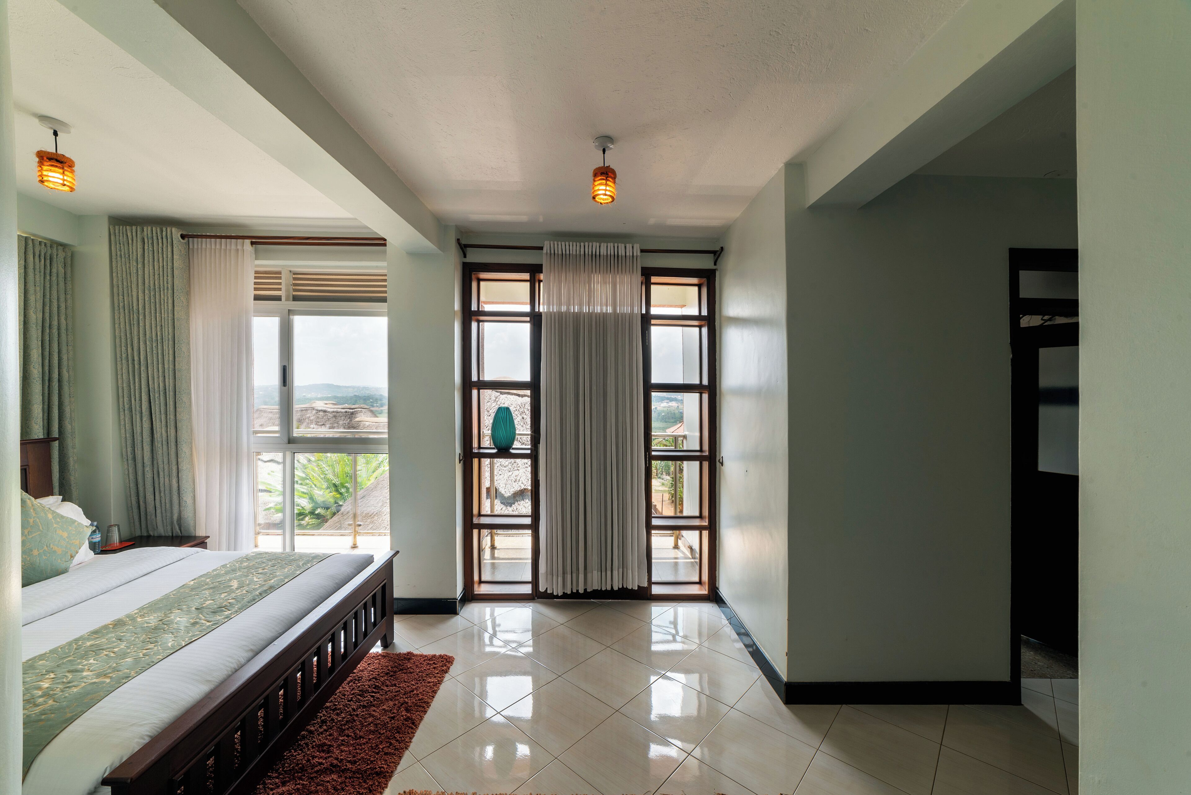 A bedroom with a large bed, a view through a glass door, and a ceiling light.