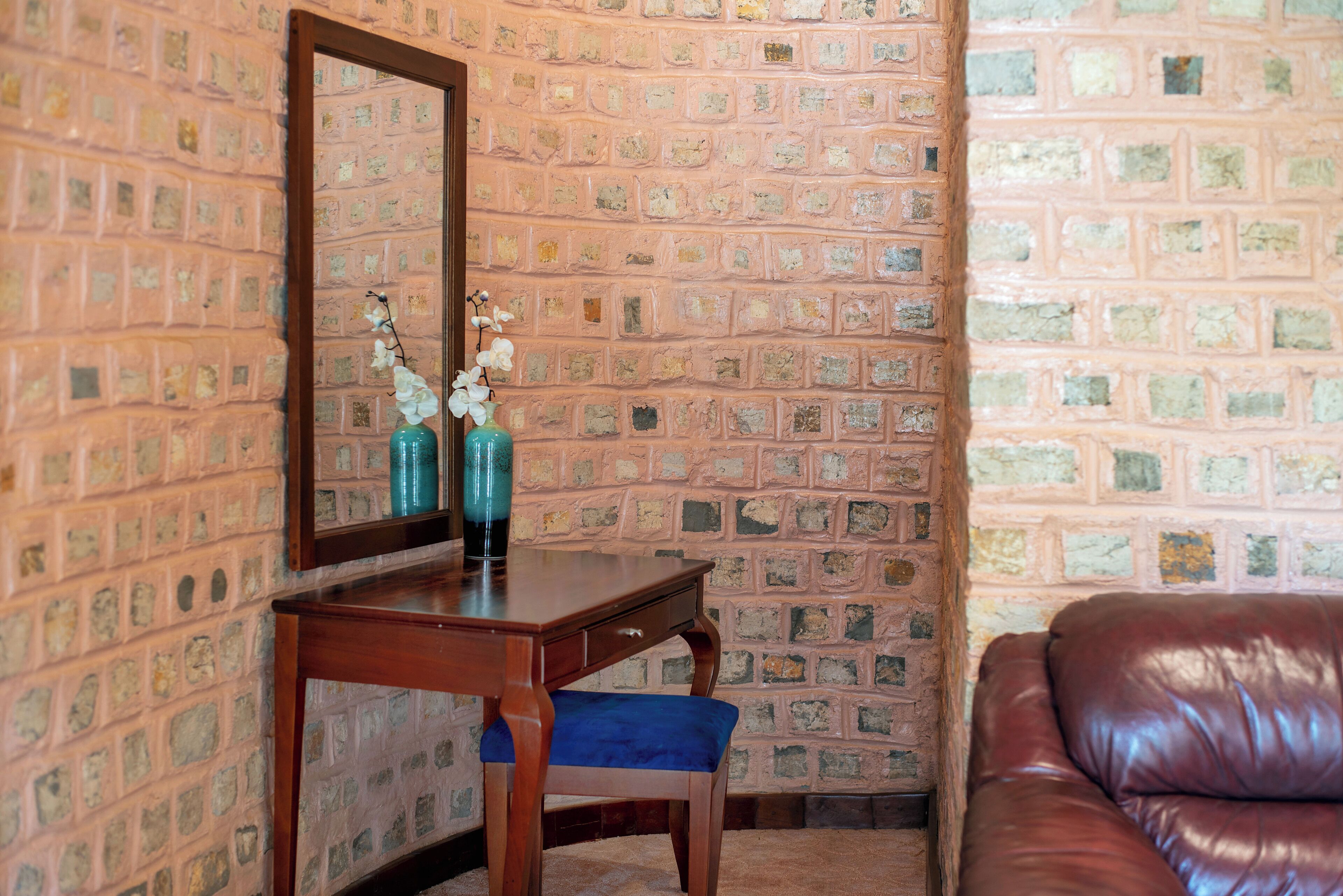 Una habitación con pared de ladrillo, un escritorio de madera con espejo, una silla tapizada en azul y un sofá de cuero marrón.