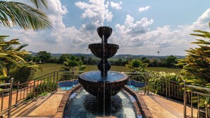 A fountain with water cascading down, surrounded by a pool and palm trees, with a view of a distant landscape. - Masheda Palms Resort (Buloba)
