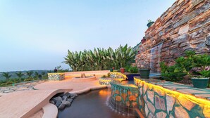 A stone-walled pool area with a waterfall feature, surrounded by potted plants and a view of the landscape. - Masheda Palms Resort (Buloba)