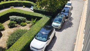 Ein Parkplatz mit mehreren Autos, darunter ein weißer Range Rover, und ein gepflegter Garten mit Hecken und einer Bank.