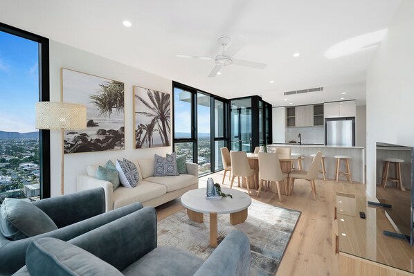 A modern living room with a sofa, coffee table, and a dining area with chairs and a kitchen in the background.