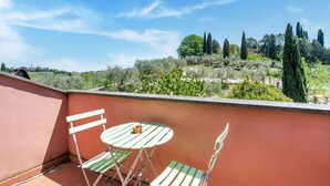 A balcony with a table and chairs, overlooking a garden with trees and shrubs.