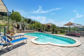 A swimming pool with lounge chairs and umbrellas, surrounded by greenery and a stone wall. - Villa in Monterotondo with Pool & Tiber Views (Monterotondo)