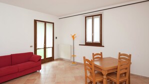 A room with a red sofa, wooden dining table with chairs, a radiator, and a window with curtains. - Belvilla by OYO Appartamento Yassine (Tredozio)