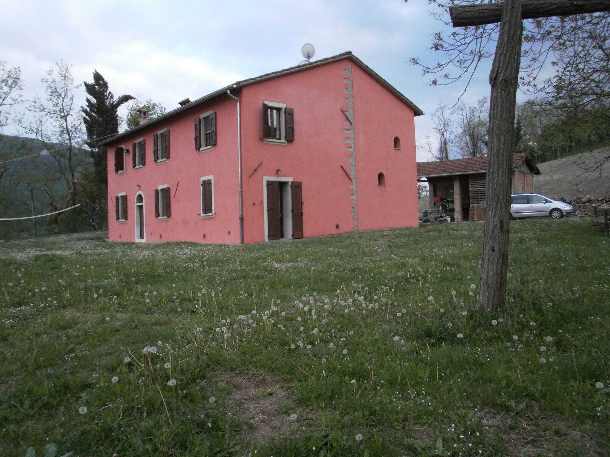 Un bâtiment rose doté de nombreuses fenêtres et d’une porte, entouré d’une pelouse et d’arbres.