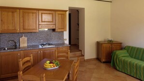 A compact kitchen with wooden cabinets, a granite countertop, and a dining table with a fruit bowl. A small wooden cabinet and a green-striped sofa are also visible. - Belvilla by OYO Appartamento Yassine (Tredozio)