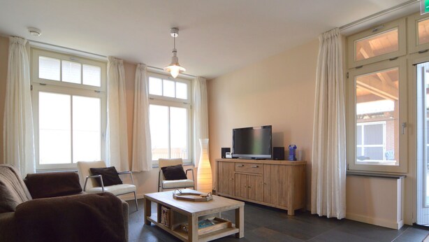 Ein Wohnzimmer mit einer Couch, Sesseln, einem Couchtisch, einem Fernseher und einem Schrank.
