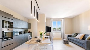 Eine moderne Küche mit Einbauofen und Mikrowelle, ein Essbereich mit Tisch und Stühlen, ein Sofa und ein Fernseher.