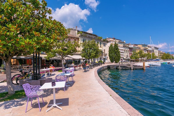 A waterfront café with outdoor seating, a dock, and boats in the background.
