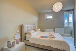 A bedroom with a large bed, bedside lamps, a bedside table, and a window with a view.