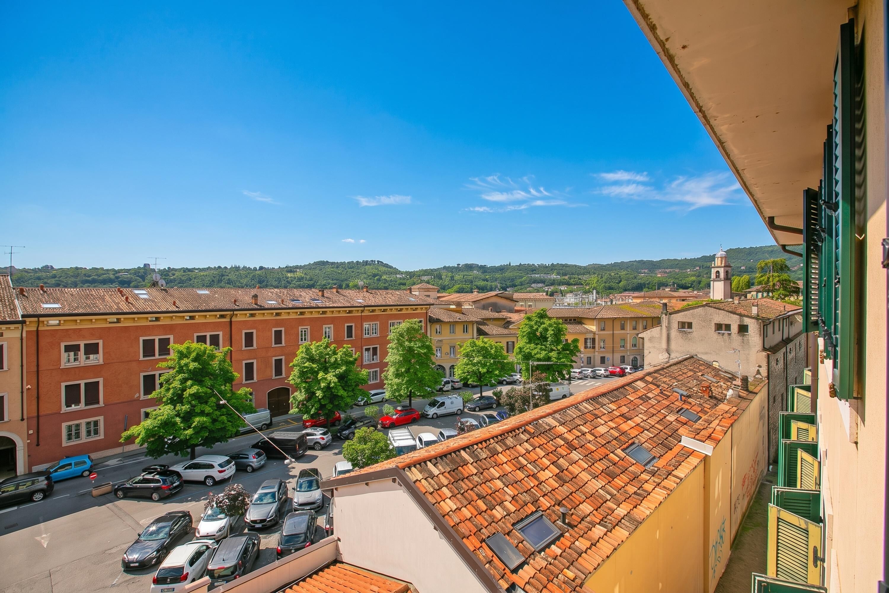 Une vue depuis un balcon donnant sur une rue bordée de voitures garées et d’immeubles.