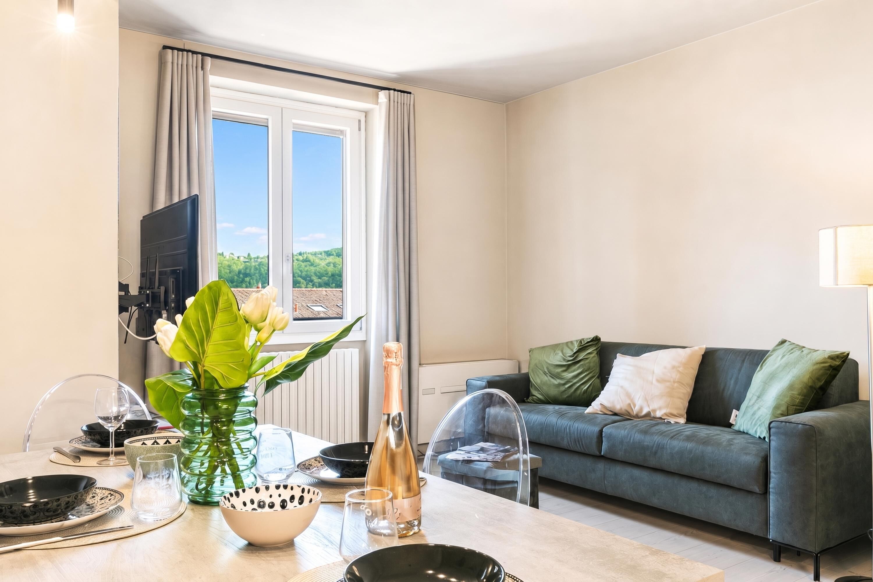 Un salon moderne avec un canapé, une table à manger dressée avec des assiettes, des verres et un vase de fleurs.