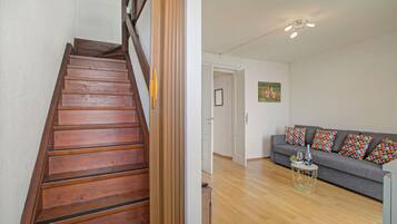 A wooden staircase leading to a room with a grey sofa, a small round table, and a painting on the wall.