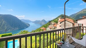 A balcony with a pool, a table with a bottle and glasses, and a view of a lake and mountains.