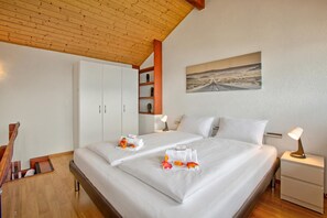 Ein Doppelbett mit weißer Bettwäsche, ein Nachttisch mit Lampe, ein Kleiderschrank und ein Gemälde einer Straße an der Wand.
