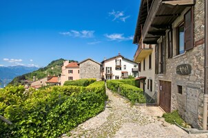 Una calle adoquinada en un pueblo en la ladera de una colina, con edificios de piedra y abundante vegetación.