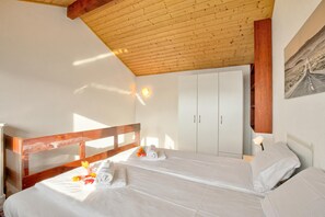 Ein Schlafzimmer mit zwei Betten, Holzbalkendecke, einem weißen Kleiderschrank und einem Bild an der Wand.