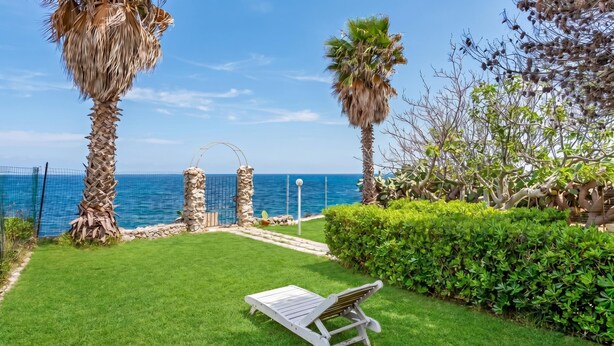 A well-maintained garden with a lounge chair, palm trees, and a view of the sea. - La Porta Sul Mare - Sea-view Home With Private Beach Access (Diso)