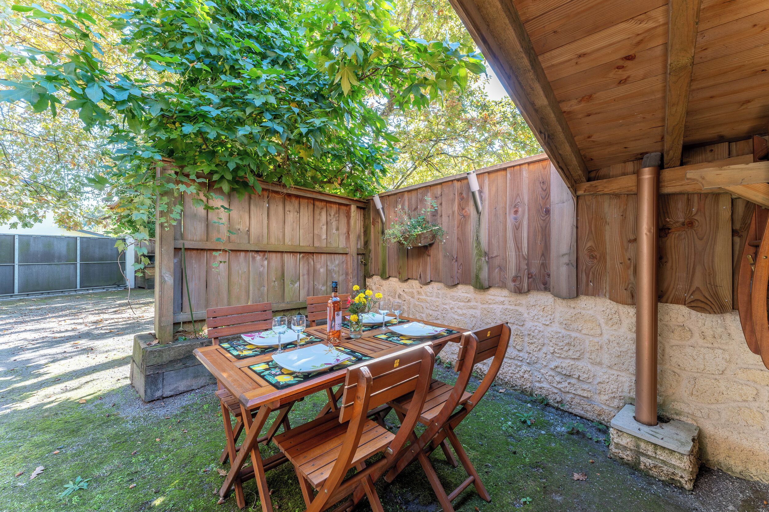 An outdoor wooden deck with a table set for dining, surrounded by stone walls and a wooden fence.