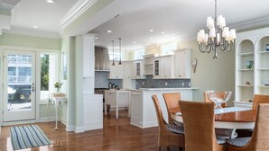 A spacious kitchen with white cabinetry, a central island, and a dining area with wicker chairs.