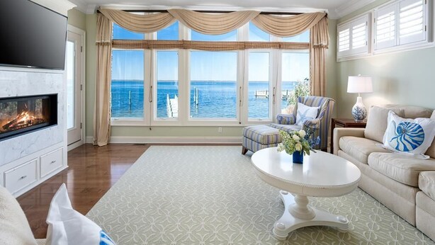 A spacious living room with a fireplace, a large window with a view of the sea, a comfortable seating area, and a flat-screen TV.
