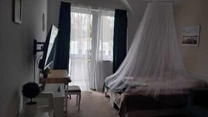 Een slaapkamer met een bed, een bureau, een stoel en een raam met gordijnen.