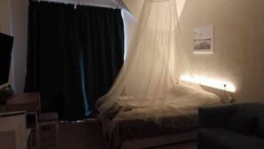 Een slaapkamer met een bed onder een baldakijn, een nachtkastje en een stoel.