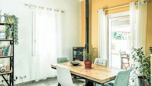 Uma sala de jantar com mesa de madeira, cadeiras, planta em vaso e fogão preto.