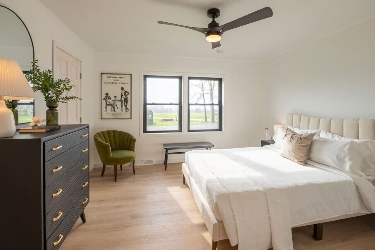 Une chambre à coucher avec un lit, une commode, une chaise et un ventilateur de plafond.