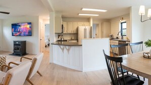Une cuisine moderne avec des meubles blancs, un îlot central et un coin repas comprenant une table et des chaises en bois.