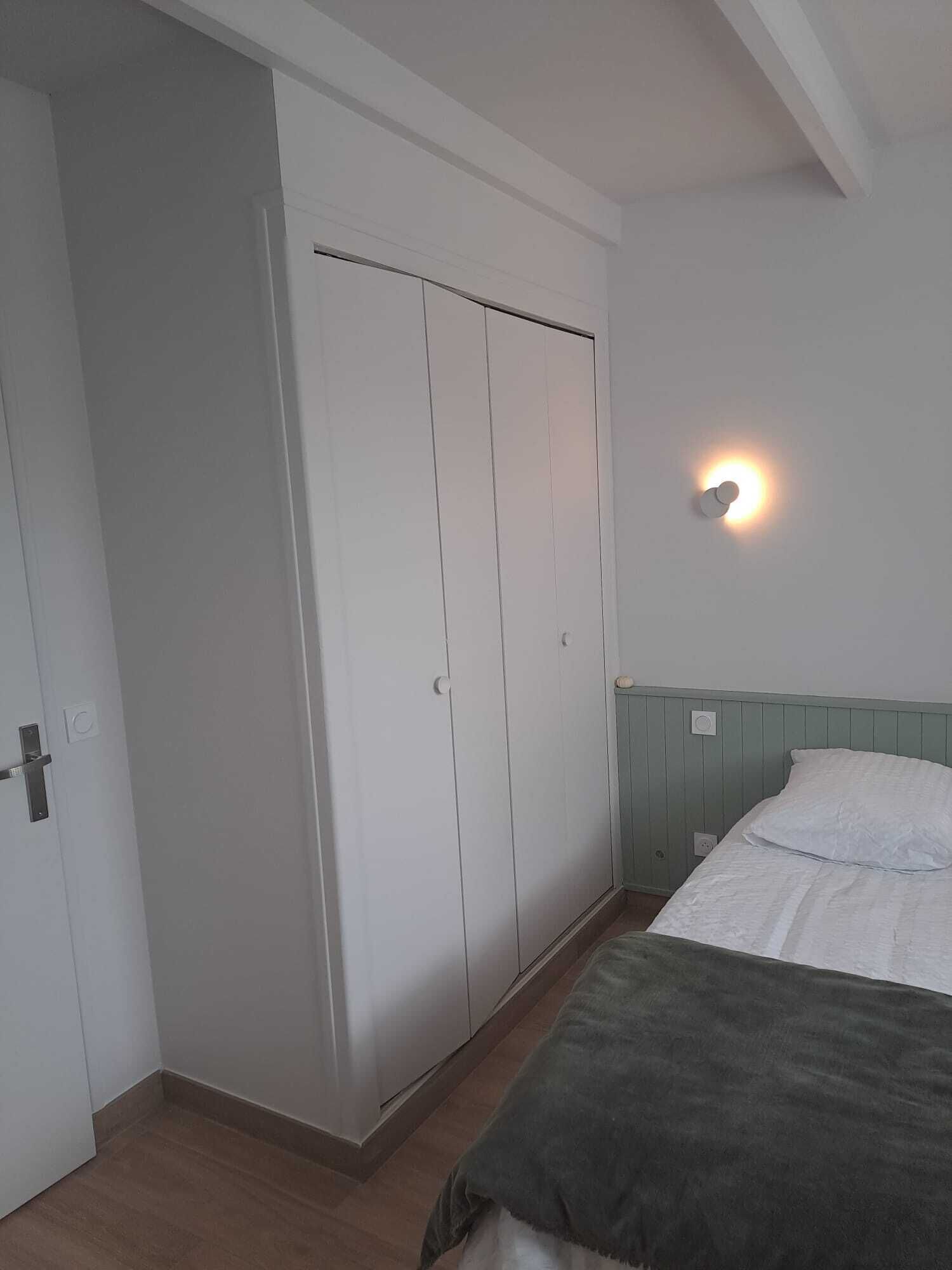 Un dormitorio con una cama, un armario y una lámpara fijada a la pared.