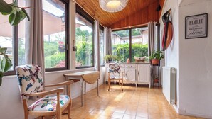 A cozy kitchen with wooden cabinets, a dining area with chairs, and large windows offering a view of the garden.