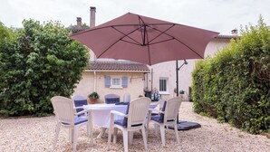 An outdoor seating area with a table and chairs, a large umbrella, and a gravel ground.